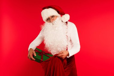 Noel Baba şapkalı, hediyeyi çuvala koyuyor kırmızıda izole edilmiş. 