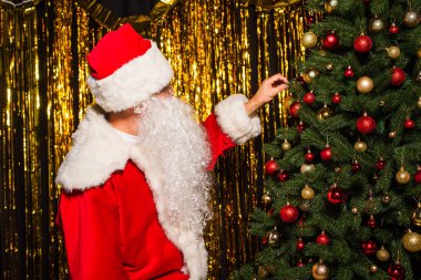 Santa claus decorating christmas tree near golden tinsel  clipart