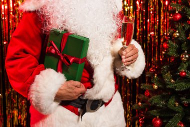 Sakallı Noel Baba 'nın elinde şampanya ve hediye kutusuyla noel ağacının yanında 
