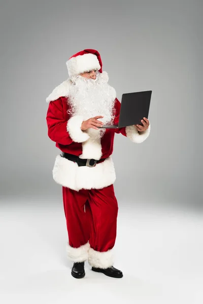 Święty Mikołaj Kostiumie Pomocą Laptopa Szarym Tle — Zdjęcie stockowe