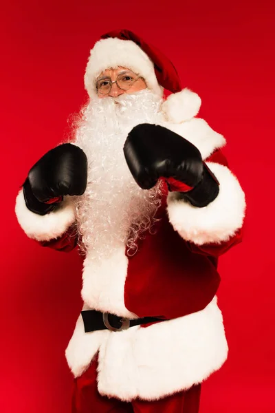 Father christmas in boxing gloves standing in fighting pose on red background