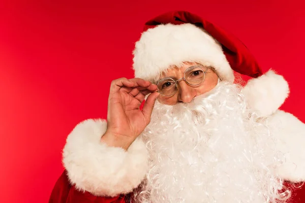 Προσωπογραφία Του Γενειοφόρου Santa Claus Αγγίζοντας Γυαλιά Που Απομονώνονται Κόκκινο — Φωτογραφία Αρχείου