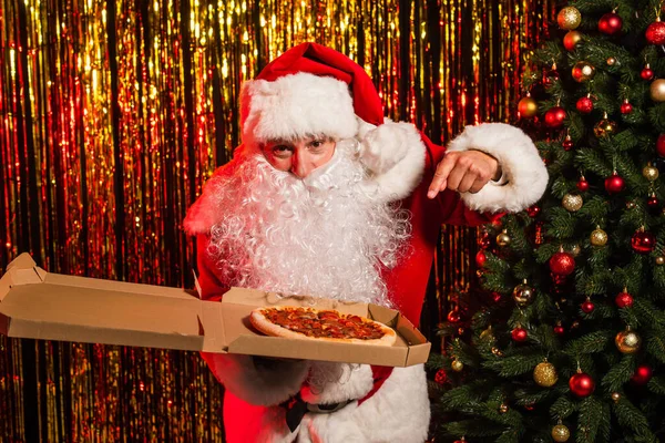 Father christmas pointing at takeaway pizza in box near festive tinsel