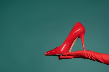 Kırmızılı kadın yeşil arka planda yüksek topuklu ayakkabı tutuyor.