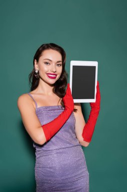 Mor elbiseli ve eldivenli mutlu genç kadın yeşil ekranlı dijital tablet tutuyor.