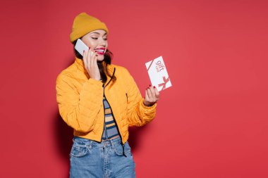 Bereli mutlu kadın ve turuncu kabarık ceketli. Elinde hediye kartı var. Kırmızı telefonda akıllı telefonla konuşuyor.