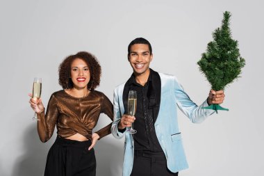 Şampanyalı şık Afrikalı Amerikalı çift ve gri arka planda küçük noel ağacı.  