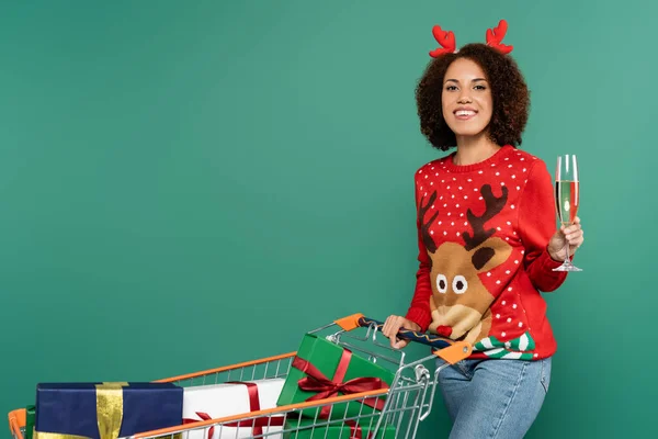クリスマスの衣装を着たアフリカ系アメリカ人の女性がショッピングカートの近くでシャンパングラスを持ち — ストック写真