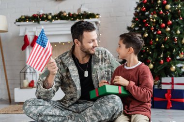 ABD bayrağını elinde tutan bir asker ve evinde süslü bir Noel ağacı.