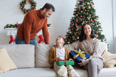 Mutlu adam oğluna bakıyor. Annesinin yanında oturuyor ve Noel hediyeleri alıyor.