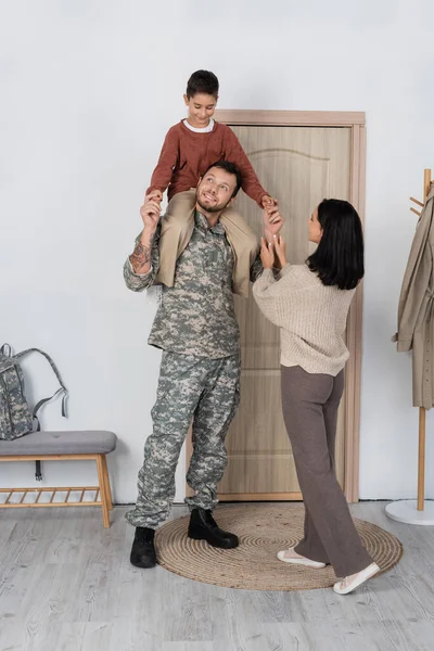 Smiling Boy Piggybacking Dad Military Uniform Wife Entrance Door Home — Stock Photo, Image