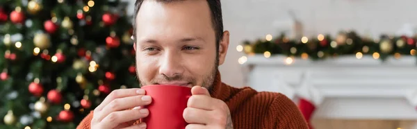 pleased man drinking warm cocoa on christmas day at home, banner