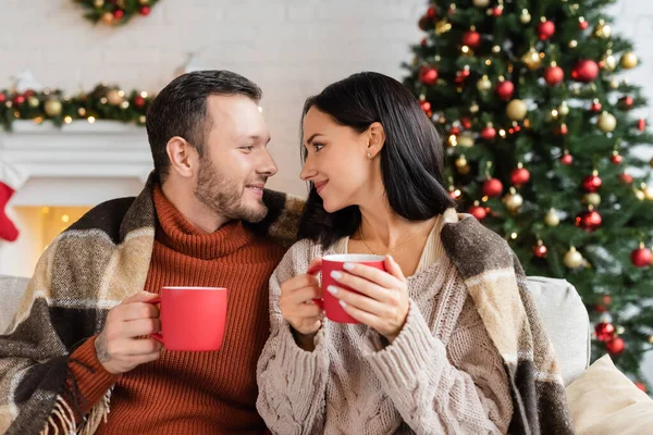 Vrolijk Paar Met Kopjes Cacao Zitten Onder Warme Deken Glimlachen — Stockfoto