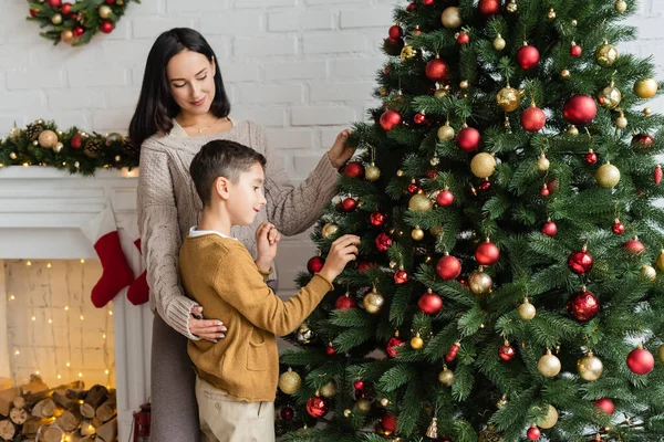 Boldog Átöleli Fia Díszítő Karácsonyfa Közel Kandalló Nappaliban — Stock Fotó