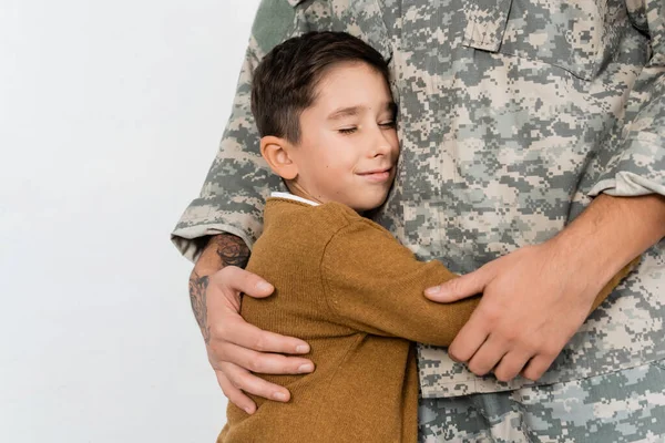 military man and his smiling son with closed eyes embracing at home