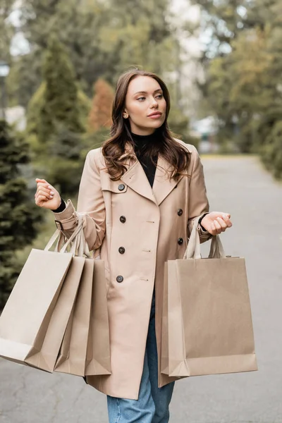 秋の公園で買い物袋を持ってるトレンチコートの若い女性 — ストック写真