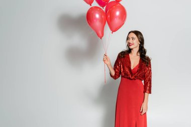 Pozitif ve şık giyinmiş bir kadın gri arka planda balonlara bakıyor. 