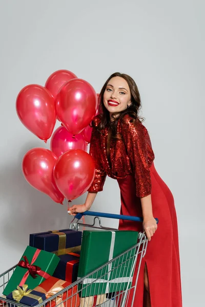 Happy Stylish Woman Standing Shopping Cart Balloons Gifts Grey Background — Stock Photo, Image