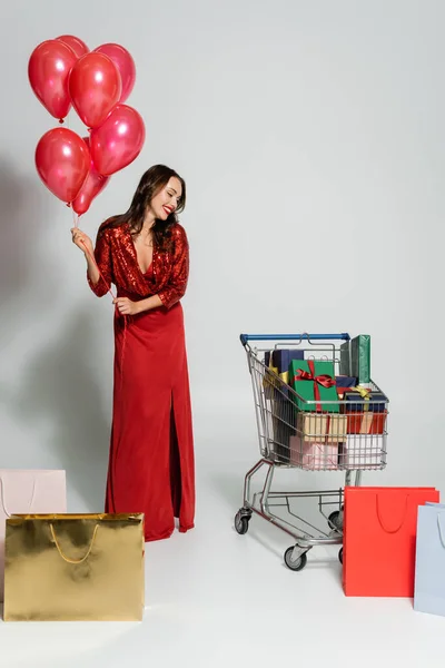 Stylish Woman Holding Balloons Shopping Bags Presents Cart Grey Background — Stock Photo, Image
