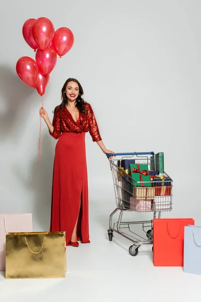 Cheerful Woman Dress Holding Balloons Shopping Cart Gifts Purchases Grey — Stock Photo, Image