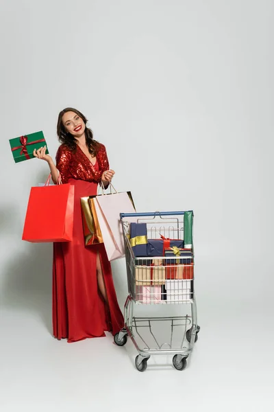 Mujer Positiva Vestido Rojo Sosteniendo Bolsas Compras Cerca Regalos Carro — Foto de Stock