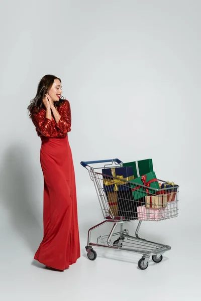 Happy Woman Elegant Dress Looking Shopping Cart Presents Grey Background — Stock Photo, Image