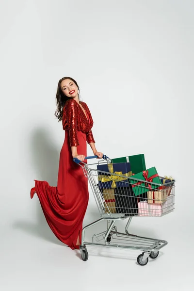 Cheerful Woman Elegant Dress Looking Camera Shopping Cart Gifts Grey — Stock Photo, Image