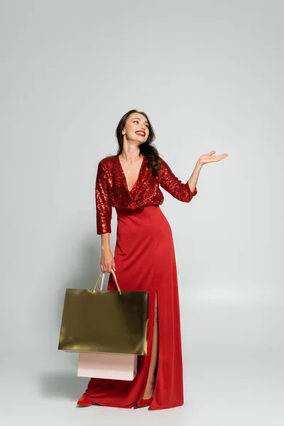 Happy Woman Red Dress Pointing Hand Holding Shopping Bags Grey — Stock Photo, Image