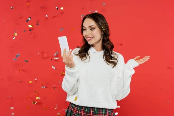 Kırmızı Arka Planda Şenlikli Konfeti Altında Akıllı Telefon Kullanan Rahat — Stok fotoğraf