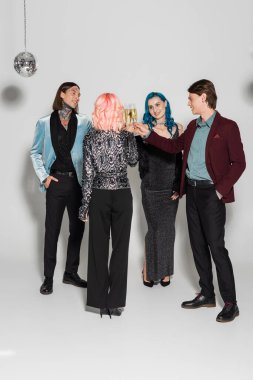 Gri arka planda şampanya kadehleri tokuşturan şık, ikili olmayan arkadaşlarla dolu.