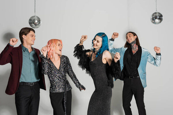возбужденные небинарные друзья в элегантной одежде танцуют на рождественской вечеринке на сером фоне