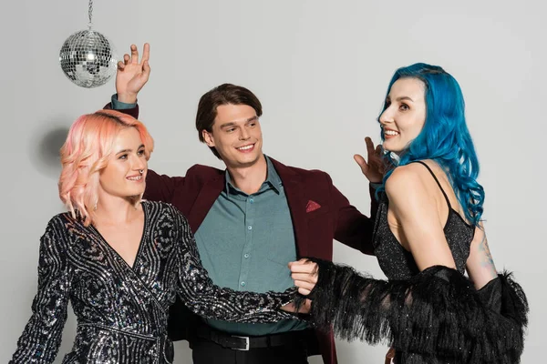 excited and stylish queer people dancing at christmas party on grey background
