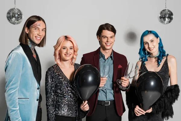 happy queer people with black balloons and champagne glasses looking at camera on grey background