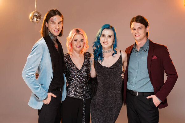 элегантные и счастливые недвоичные друзья смотрят в камеру на бежевом фоне с розовым освещением 