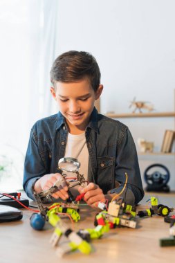 Evinde robot modelinin yanında büyüteç tutan neşeli çocuk. 