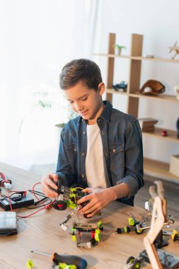 Happy preteen boy making robotic model near tools on table at home  clipart