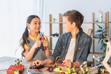 Gülümseyen kız arkadaşının yanında pense tutuyor ve evde robot modeli yapıyor. 