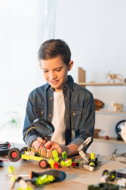 Gülümseyen çocuk evde bulanık robot modelinin yanında büyüteç tutuyor. 