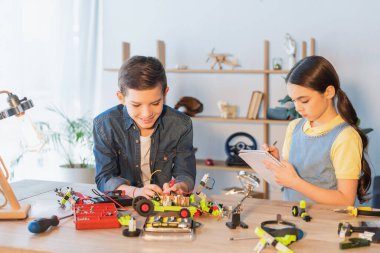 Gülümseyen çocuk evde defterine yazı yazan yakın arkadaşının robot modelini yapıyor. 
