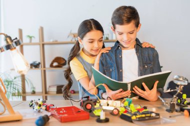 Bulanık robotik modelin yanında not defteriyle sarılan genç kız. 