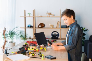 Robot modelinin detaylarının yanında büyüteç ve boş ekranlı dizüstü bilgisayar olan çocuğun yan görüntüsü