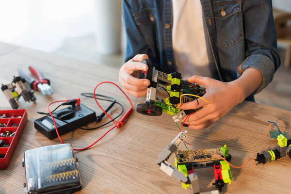 Cropped view of preteen child holding robotic model near blurred screws and millimeter at home 