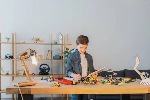 Хлопчик Тримає Цифровий Планшет Пише Блокноті Біля Механічних Деталей Моделі — стокове фото