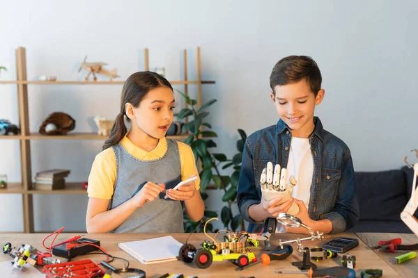 Niño Sonriente Sosteniendo Mano Robótica Cerca Chica Sorprendida Con Teléfono — Foto de Stock