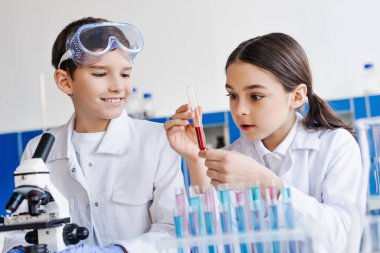 Kızın elinde kırmızı sıvı ve gülümseyen çocuğun yanında test tüpü ve laboratuarda mikroskop tutması hayret verici.