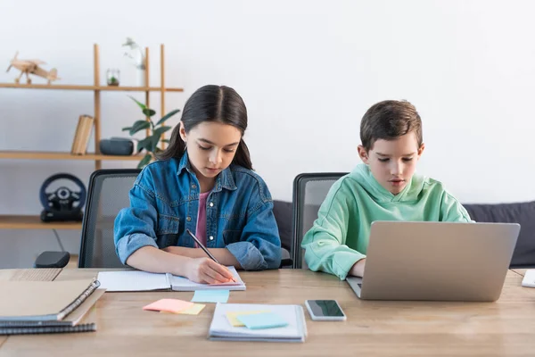 Boy Using Laptop Girl Writing Notebook Smartphone Blank Screen Desk — Stock Photo, Image