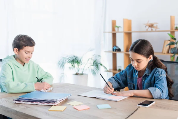 Niño Sonriente Chica Concentrada Escribiendo Cuadernos Cerca Notas Adhesivas Vacías —  Fotos de Stock