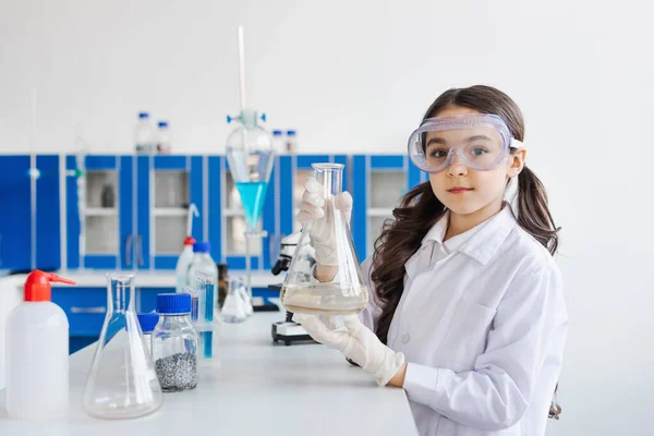 ブルネット女の子でゴーグル見てカメラと保持フラスコで化学実験室 — ストック写真