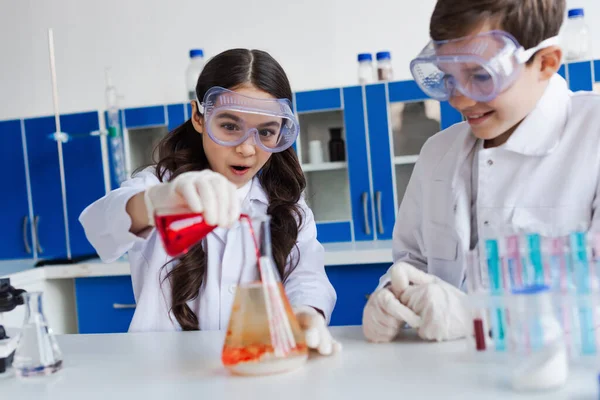 Astonished Girl Goggles Pouring Liquid Flask Chemical Experiment Smiling Friend — Stock Photo, Image