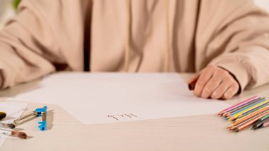 Evinde yüksek harflerle ve renkli kalemlerle kağıdın yanında oturan kadın manzarası. 